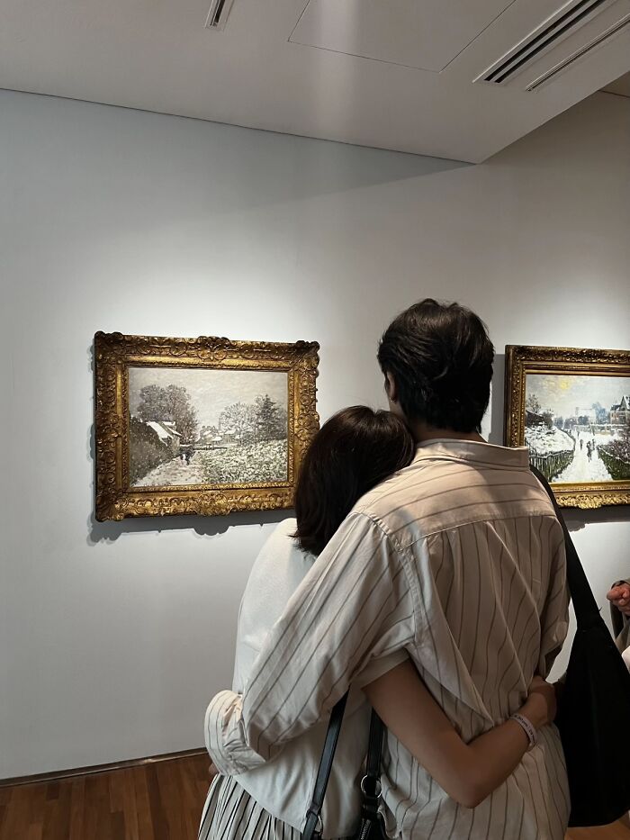 A couple from behind, embracing while looking at paintings in a museum, like a painting, wholesome photo trend.