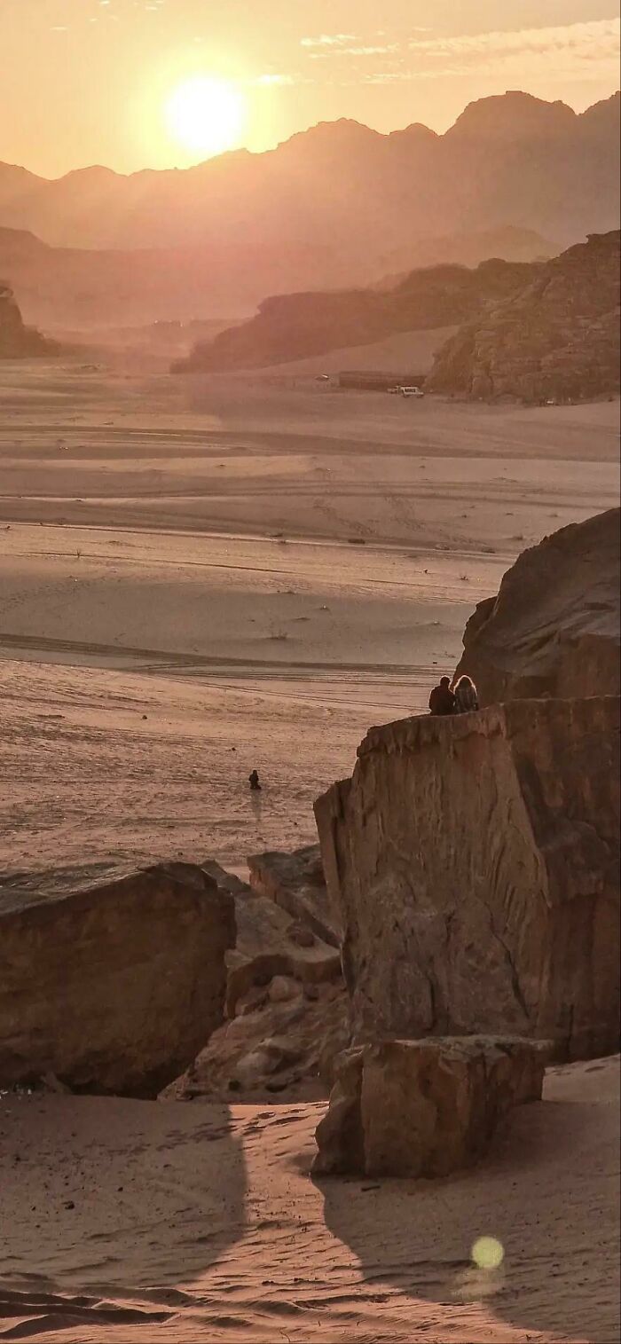 Two people silhouetted against a desert landscape at sunset, like a painting, capturing the wholesome photo trend.