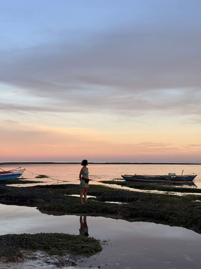 A wholesome photo trend of a woman at sunset by the water with boats, like a painting.