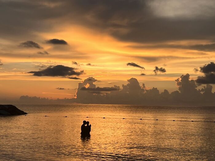 A couple embracing in the ocean at sunset, like a painting, showcasing the wholesome photo trend.