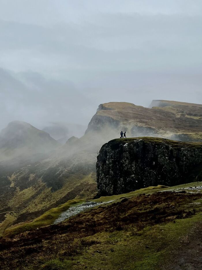 A wholesome photo trend of two strangers on a misty cliffside, resembling a painting.