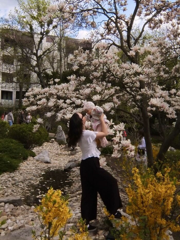 A wholesome photo trend of a woman holding a baby under a blossoming tree, like a painting.