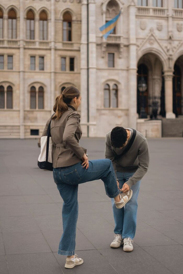 A man tying a woman's shoe in front of a grand building, a wholesome photo trend in a public space.