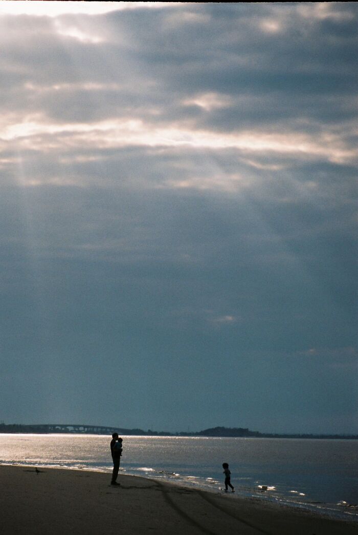 Silhouettes of a parent and child on a beach under a dramatic sky, a wholesome painting photo trend.