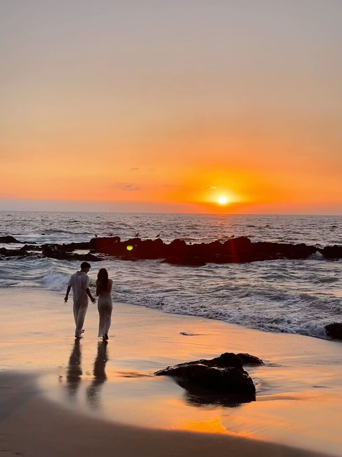 A couple walks along a beach at sunset, a wholesome photo trend of beautiful moments.