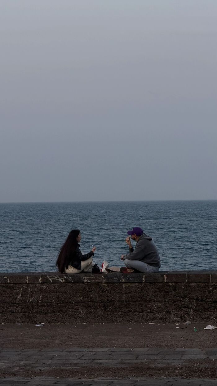 A couple sits on a sea wall enjoying the view, capturing the wholesome photo trend.
