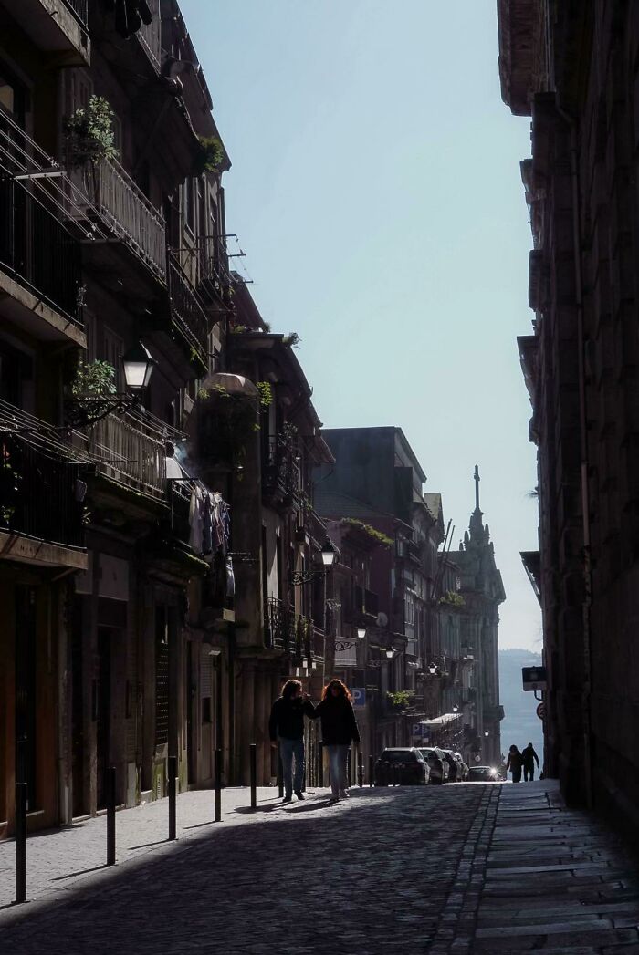 Two figures walking down a narrow street lined with buildings, an example of the 'Like A Painting' photo trend.