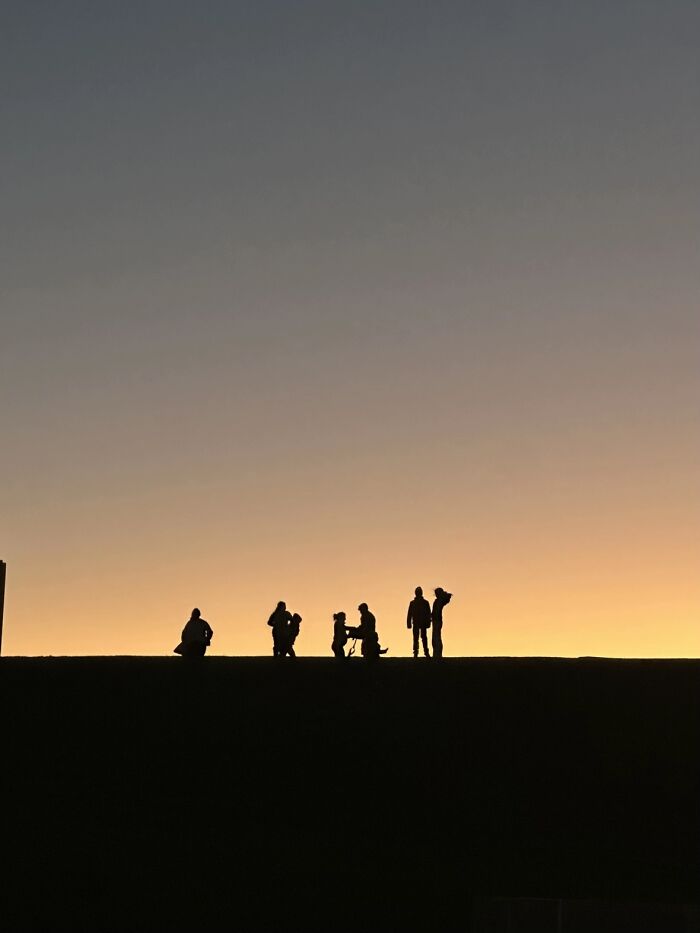 Silhouettes of people and a dog against a sunset, illustrating the 'Like A Painting' photo trend.