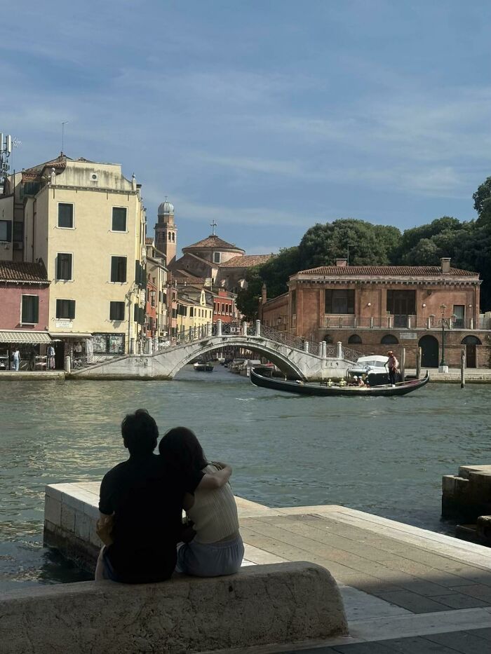 A wholesome photo of a couple embracing by a canal in Venice, embodying the 'Like A Painting' photo trend.
