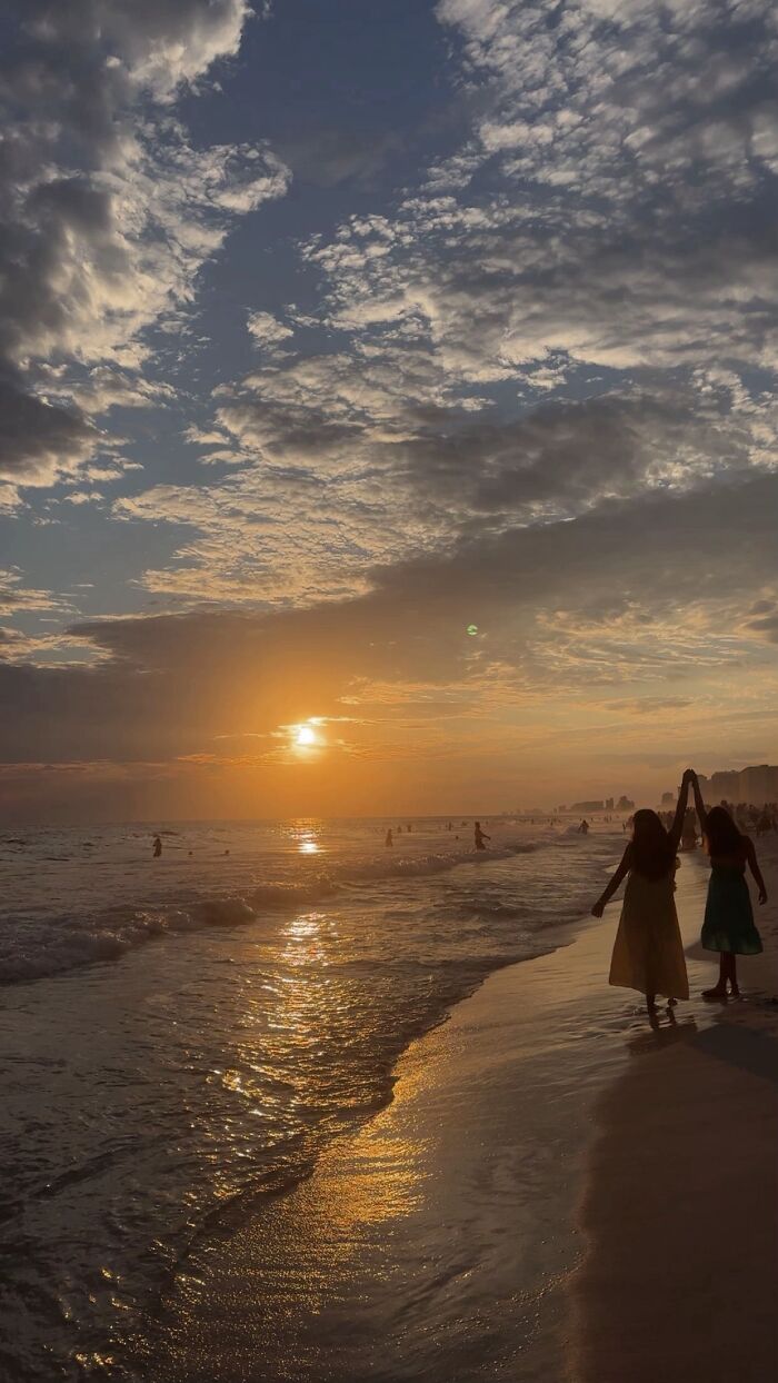 A wholesome photo of two people holding hands on a beach at sunset, reflecting the beautiful photo trend.