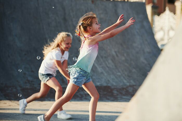 Two girls playing and chasing bubbles outdoors in sunny setting