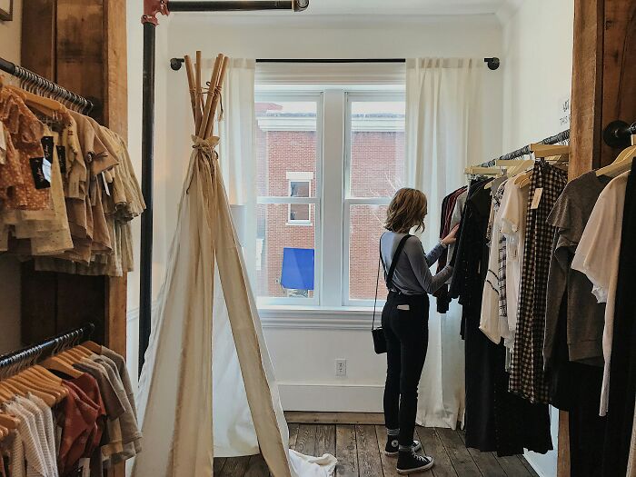 Woman browsing clothes in boutique dressing room with natural light