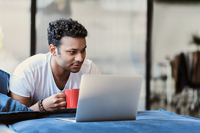 Man working remotely on laptop while holding red coffee mug