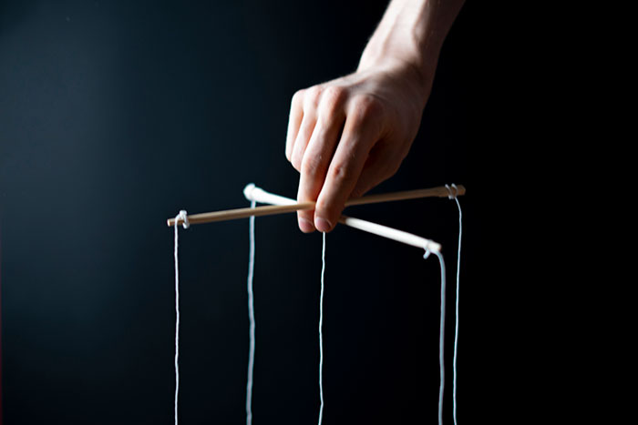 Hand holding marionette control for puppet in unusual job