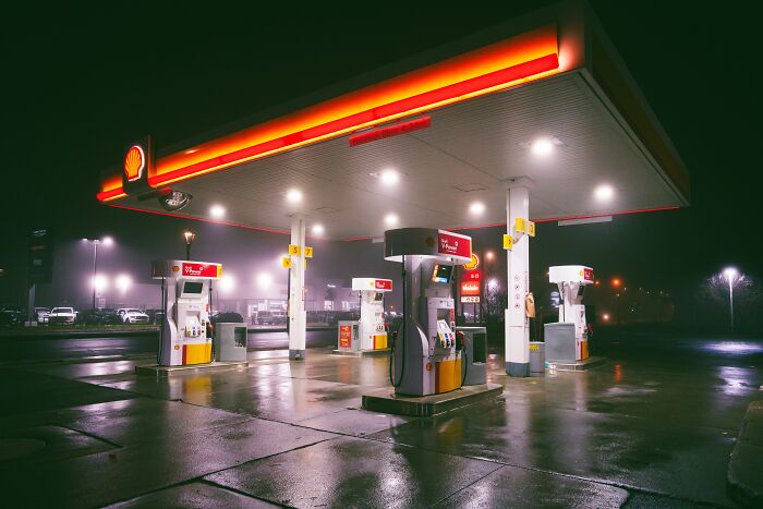 A brightly lit Shell gas station at night, with pumps and cars, featuring stories about people who hid their true selves.