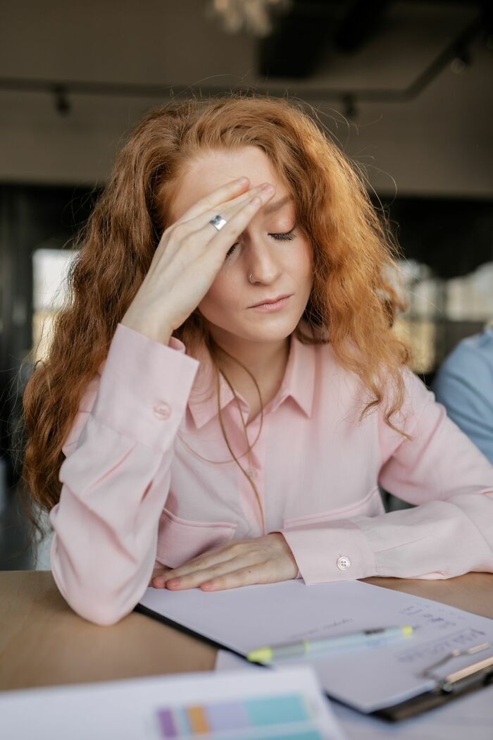 A woman with her hand on her forehead, showing a hint of deep thought, a sign a person is secretly very smart.