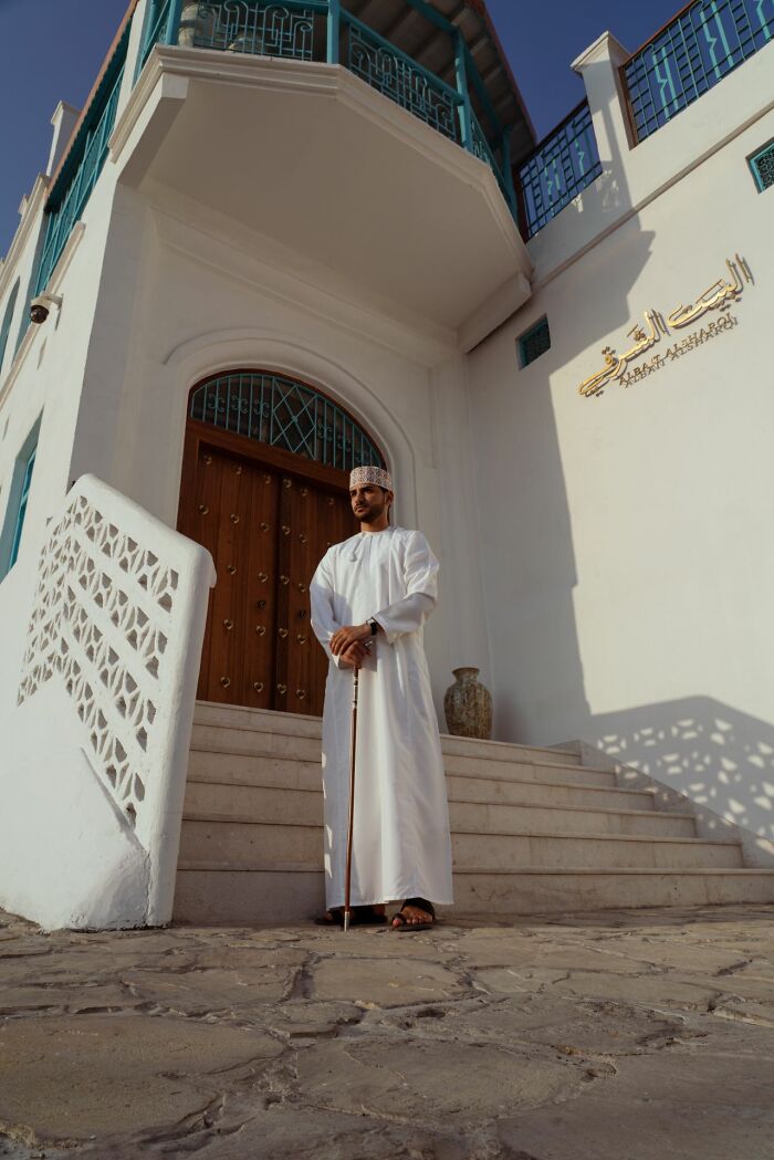A man in traditional attire stands before a white building, depicting a polygamist family context.