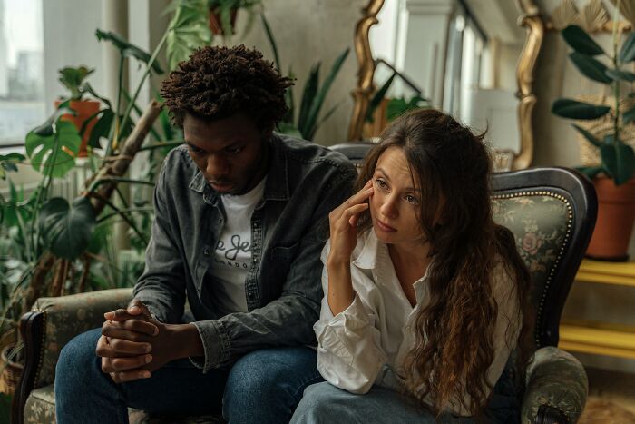 Couple sitting on sofa looking upset during tough conversation about verbal weapon against men