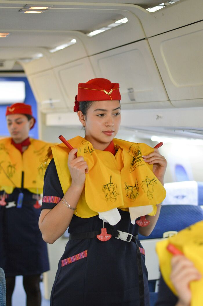 Flight attendants demonstrating safety procedures with life jackets inside airplane cabin