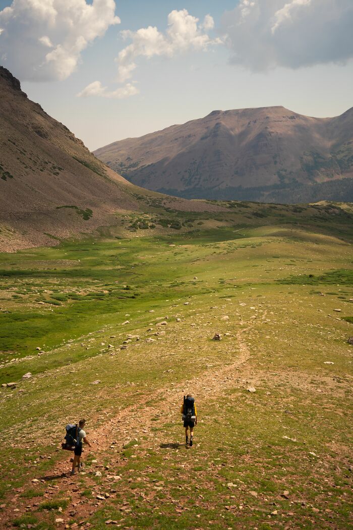 Two hikers walking through a vast mountain landscape, potentially encountering wild coincidences.