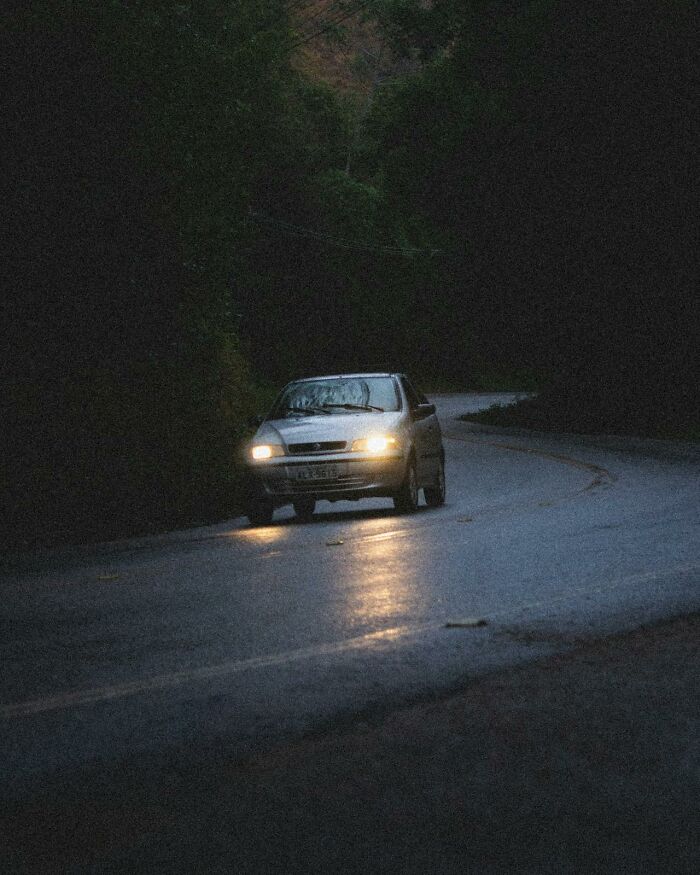 Car driving on dark winding road at night with headlights on