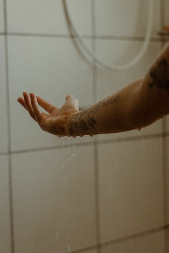 Outstretched arm with tattoos catching water drops, symbolizing the intricacies of human bodies.
