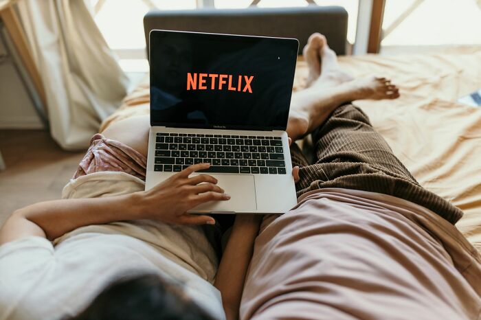 A couple relaxing on a bed watching Netflix on a laptop, illustrating surprising facts.