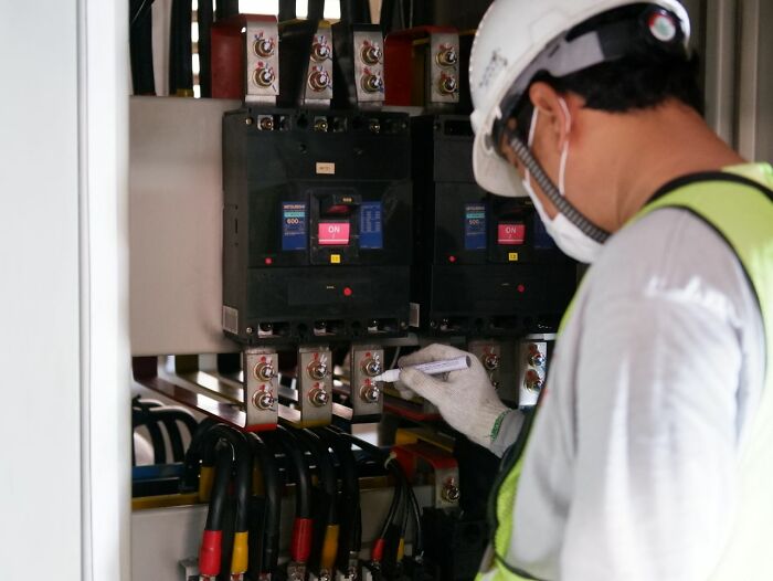 An electrician wearing a hard hat and mask, working on a fuse box, experiencing something creepy.