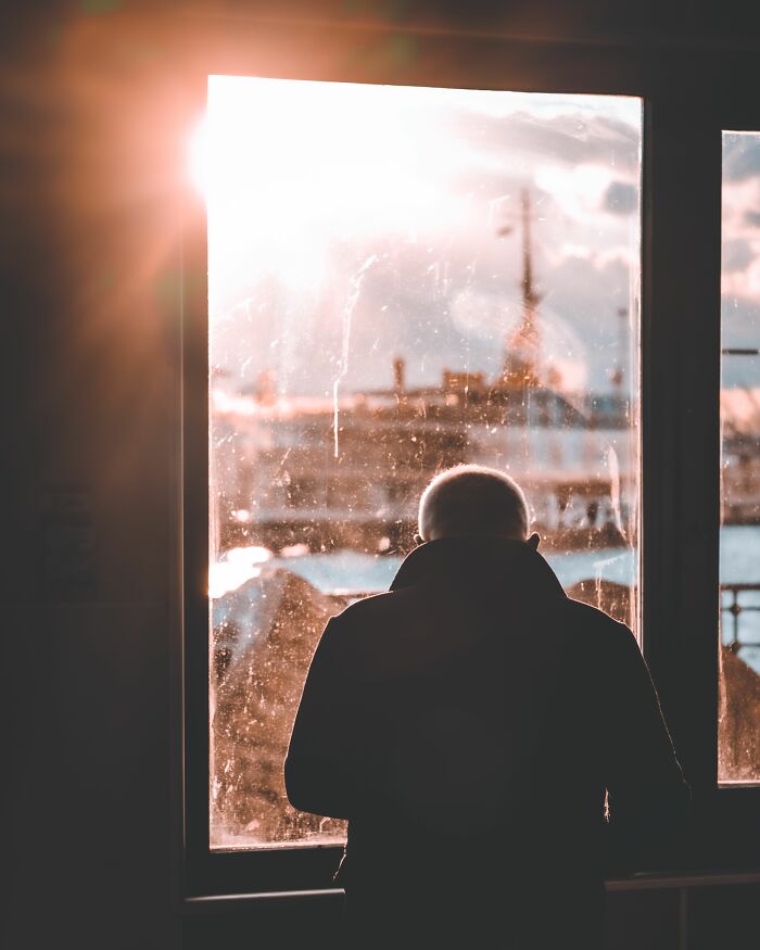 Silhouette of person looking through bright window with a cityscape outside