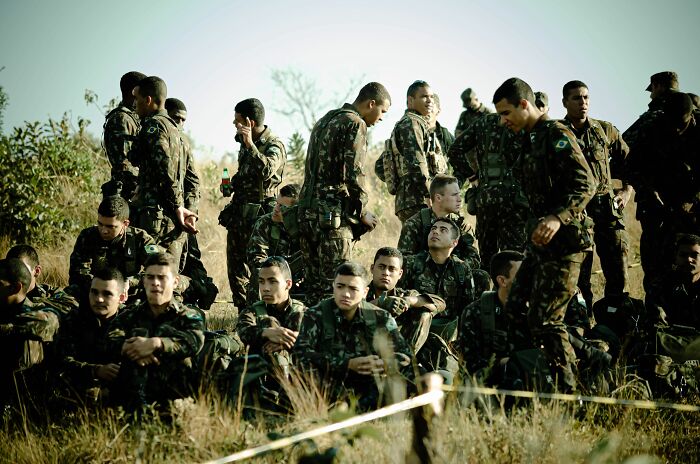 Soldiers in camouflage uniforms are seen on a grassy field, some standing, others sitting, illustrating a scene where people snapped.