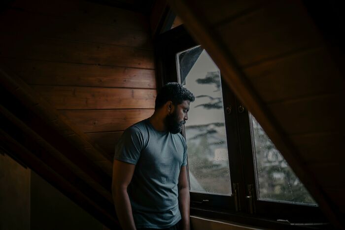 Man looking sadly out window contemplating cheating impact
