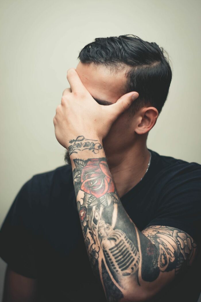A man with tattoos covers his face, possibly reacting to a wild courtroom story.