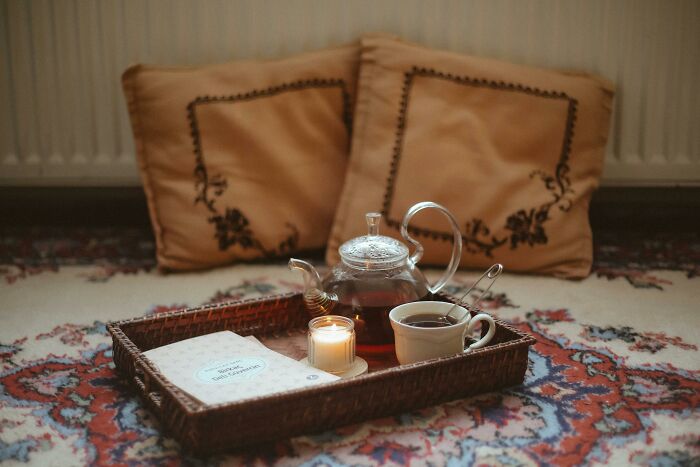 Tea set with glass teapot and candles on woven tray indoors