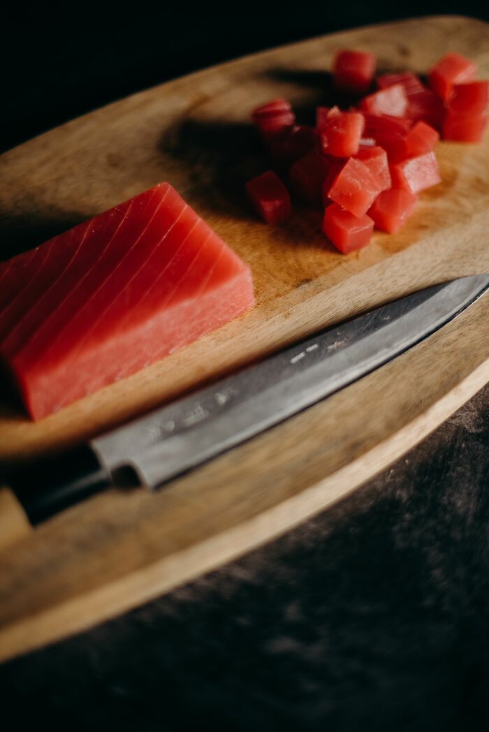 Fresh raw tuna diced on wooden cutting board with chef knife