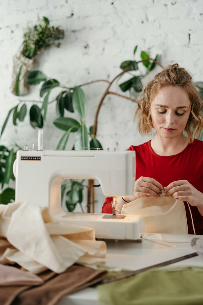 Woman sewing fabric using sewing machine in bright room