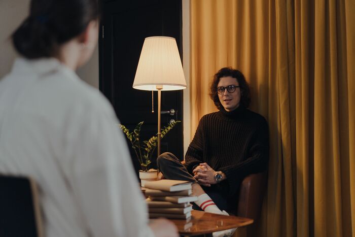 Man in glasses sitting in dimly lit room having conversation