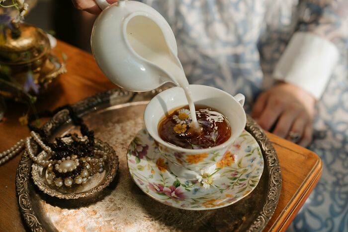 Pouring milk into a floral tea cup on a vintage tray for tea time
