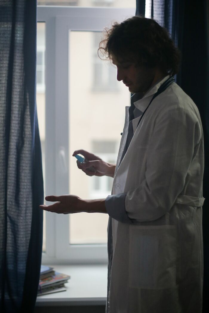 A man in a lab coat, using hand sanitizer by a window, representing true selves and the layers people hide.