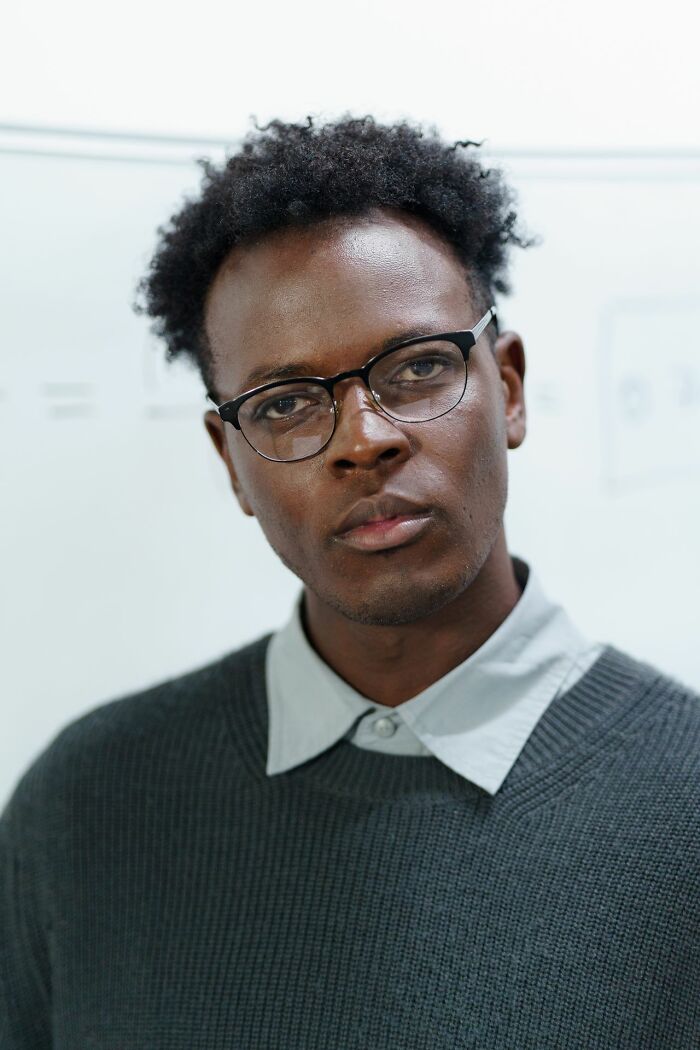 A man with curly hair and glasses looking directly at the camera, showing hints that a person is secretly very smart.