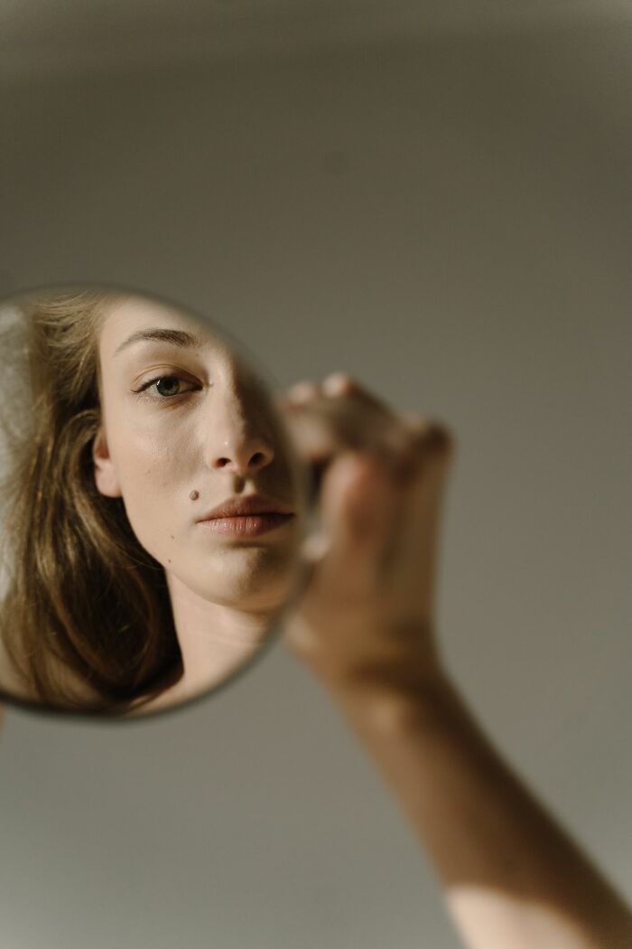 A woman holding a mirror, her reflection showing half her face, suggesting experiences people can't explain.