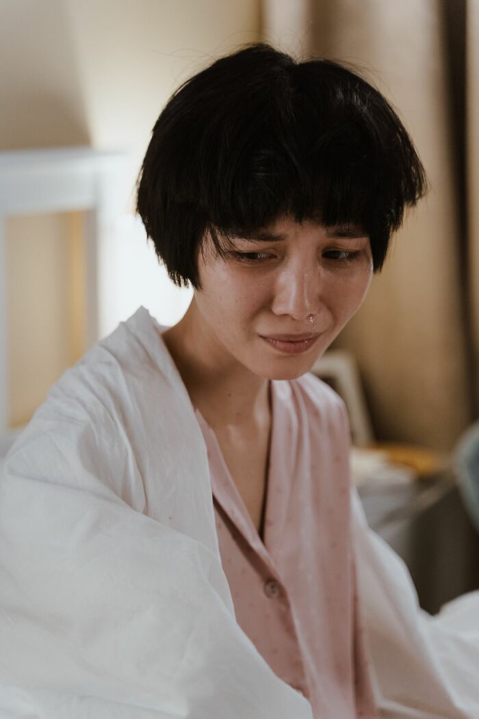 A woman sits on a bed, experiencing types of pain she won't comprehend until she's suffered through them.