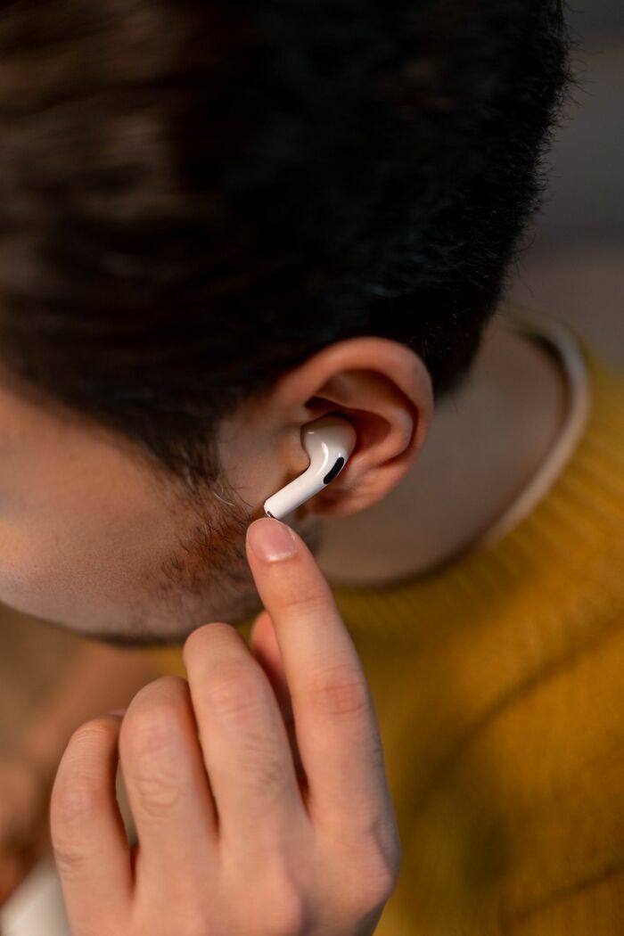 A person inserting a white earbud into their ear, suggesting a common, minor issue unrelated to serious ER visits.