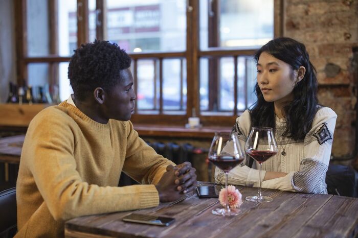 Two people at a cafe table, looking at each other, perhaps discussing a creepy, unbelievable experience.