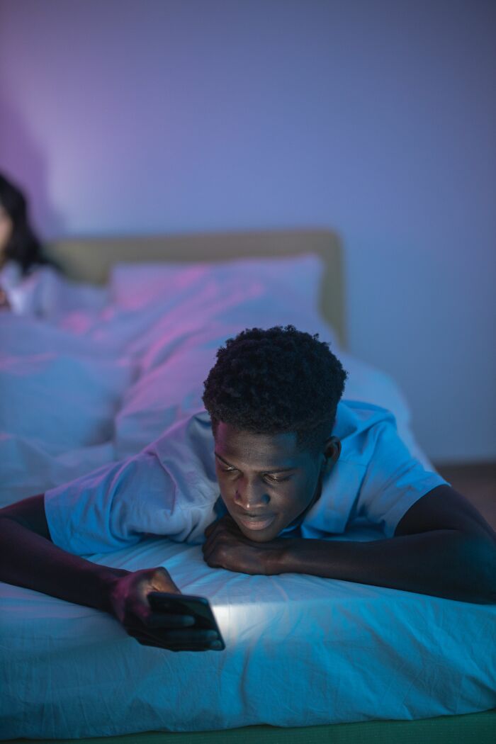 Man lying on bed at night looking at smartphone screen