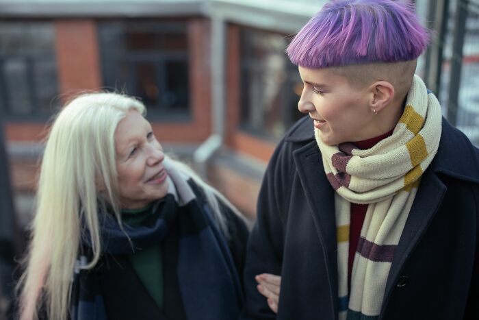 Two women, one with long blonde hair and another with short purple hair, walking together and looking at each other. A wild coincidence.