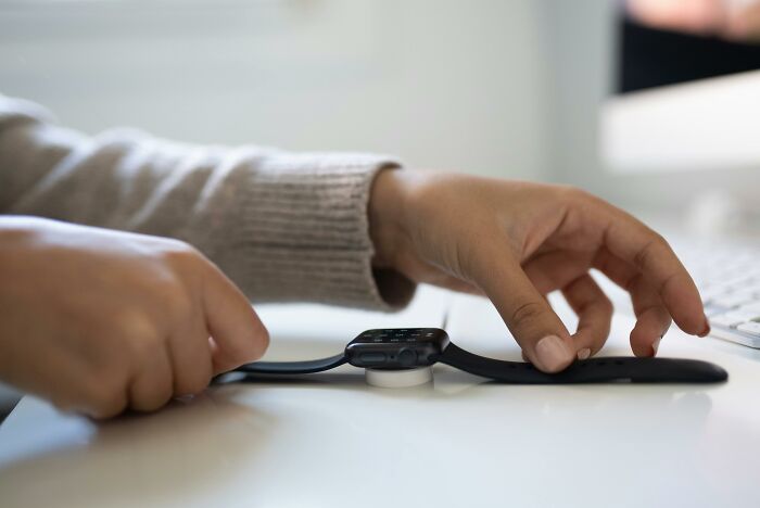 Person placing smartwatch on charger beside keyboard