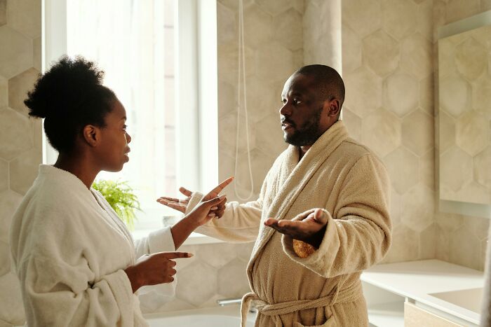 Couple in bathrobes arguing in bathroom with expressive gestures