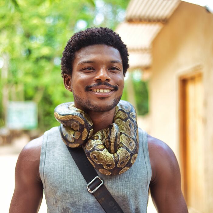 A man smiling with a snake around his neck, an unusual experience for those visiting the US.