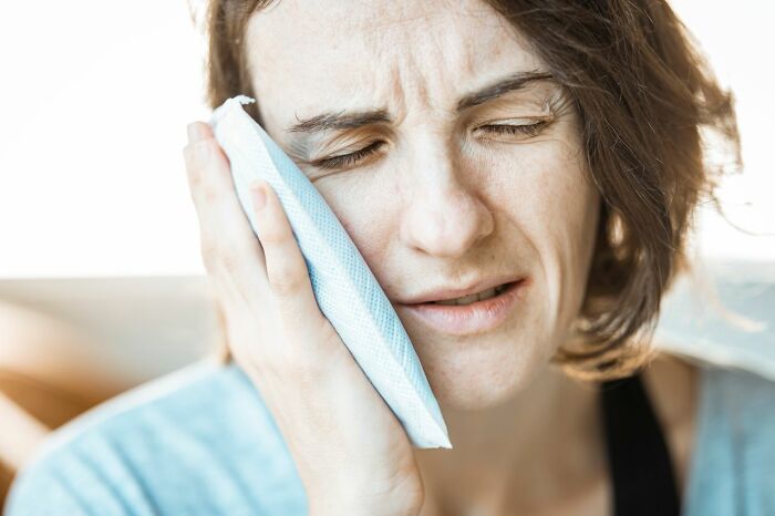 Woman with an ice pack on her cheek, depicting types of pain.