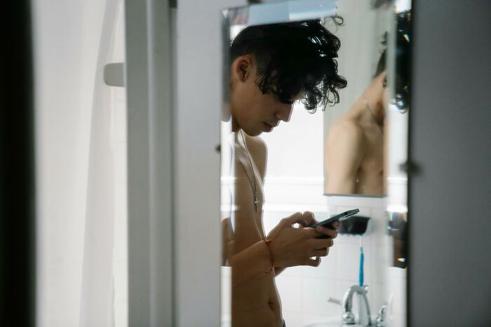 Shirtless man looking at phone in bathroom mirror